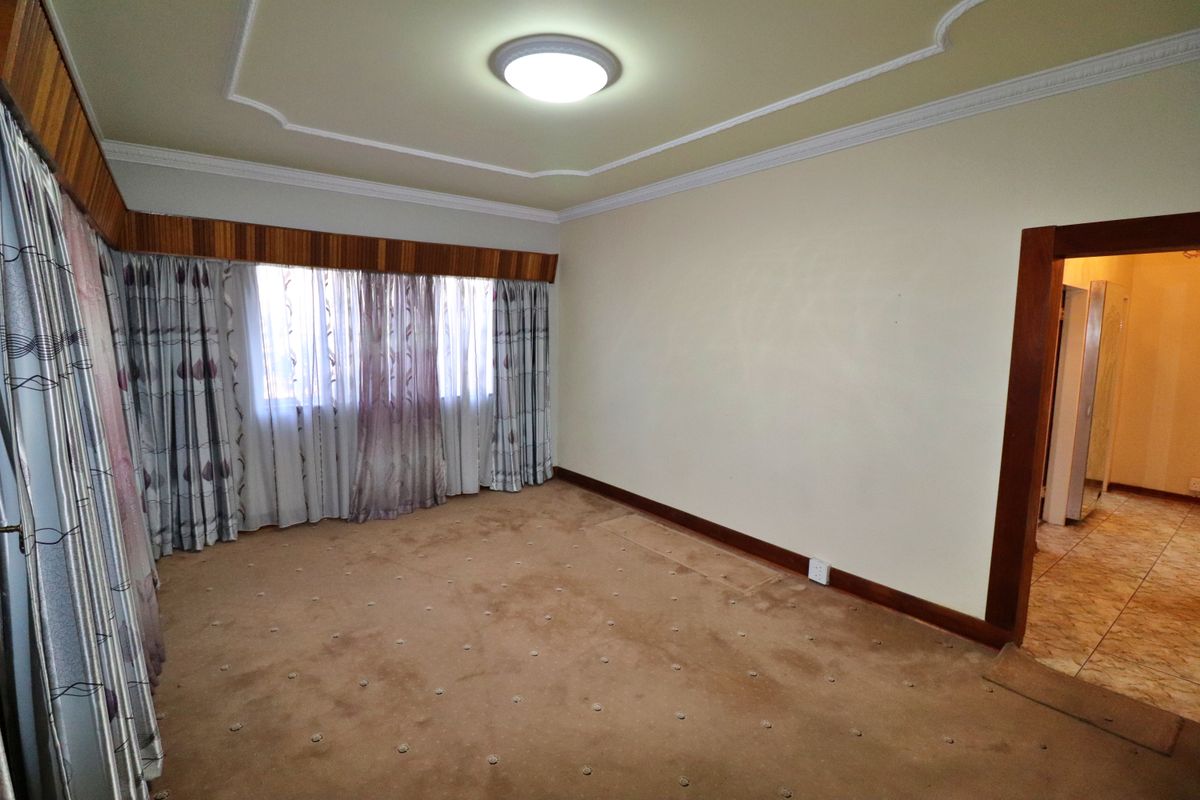 A spacious, empty bedroom featuring carpeted flooring, decorative ceiling molding, and a wooden window pelmet, offering a blank canvas for personalization.