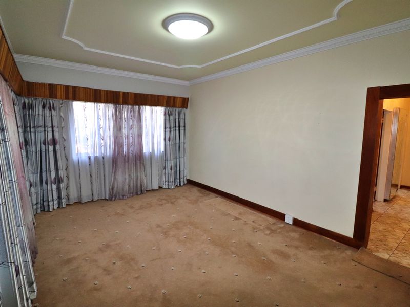 A spacious, empty bedroom featuring carpeted flooring, decorative ceiling molding, and a wooden window pelmet, offering a blank canvas for personalization.