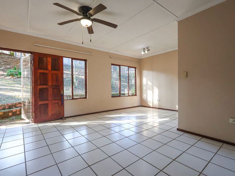 Spacious, empty living area featuring tiled flooring, a ceiling fan, and direct access to the rear garden through a timber door.