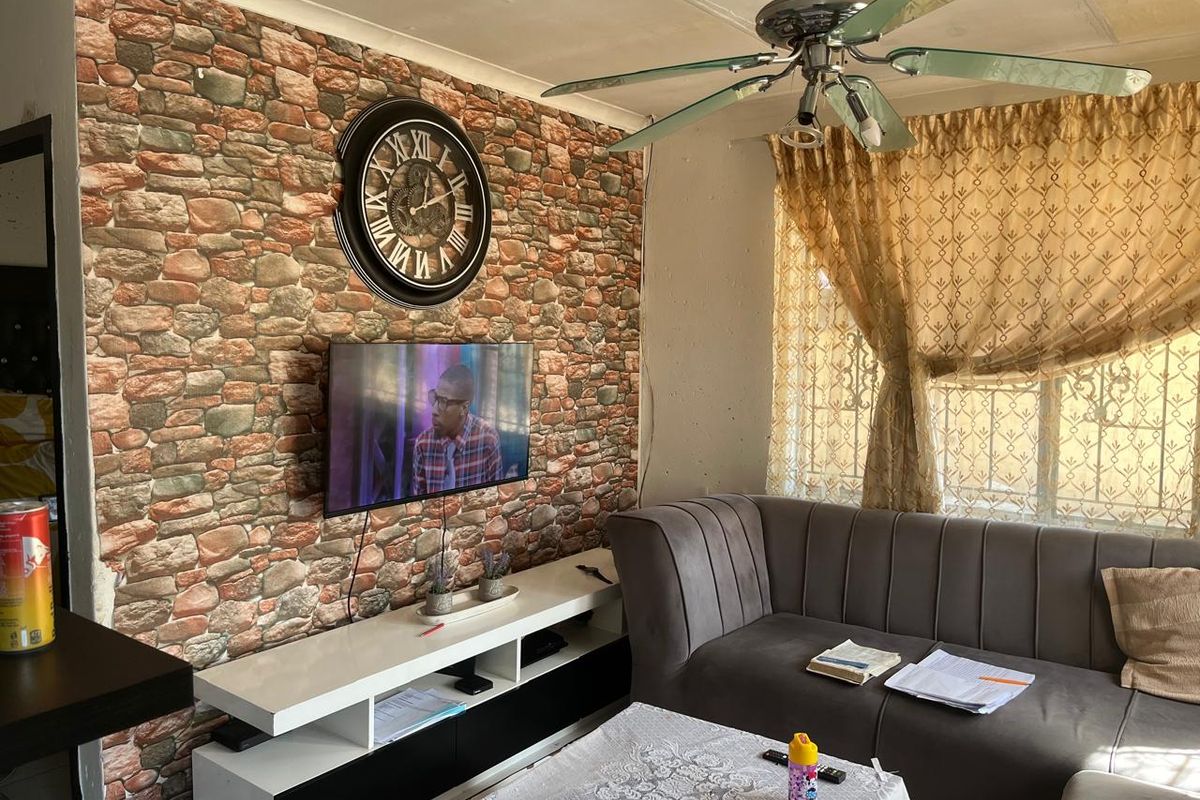 Living room featuring a faux stone accent wall, ceiling fan, and security bars on the window.