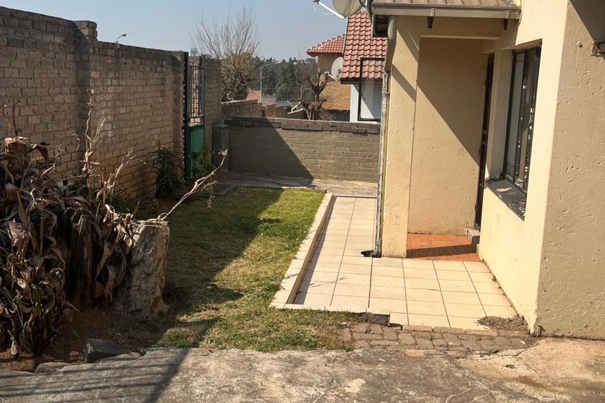 Rear exterior view of the property featuring a small tiled patio, concrete driveway, and brick boundary wall with a satellite dish mounted on the roof.