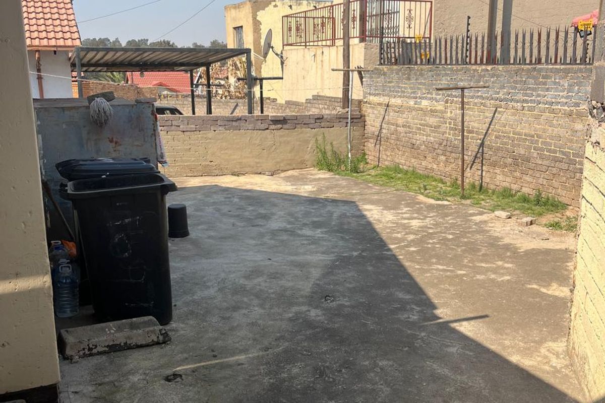 A rear exterior yard area featuring concrete paving, a brick boundary wall, and a metal washing line, requiring maintenance and landscaping improvements.