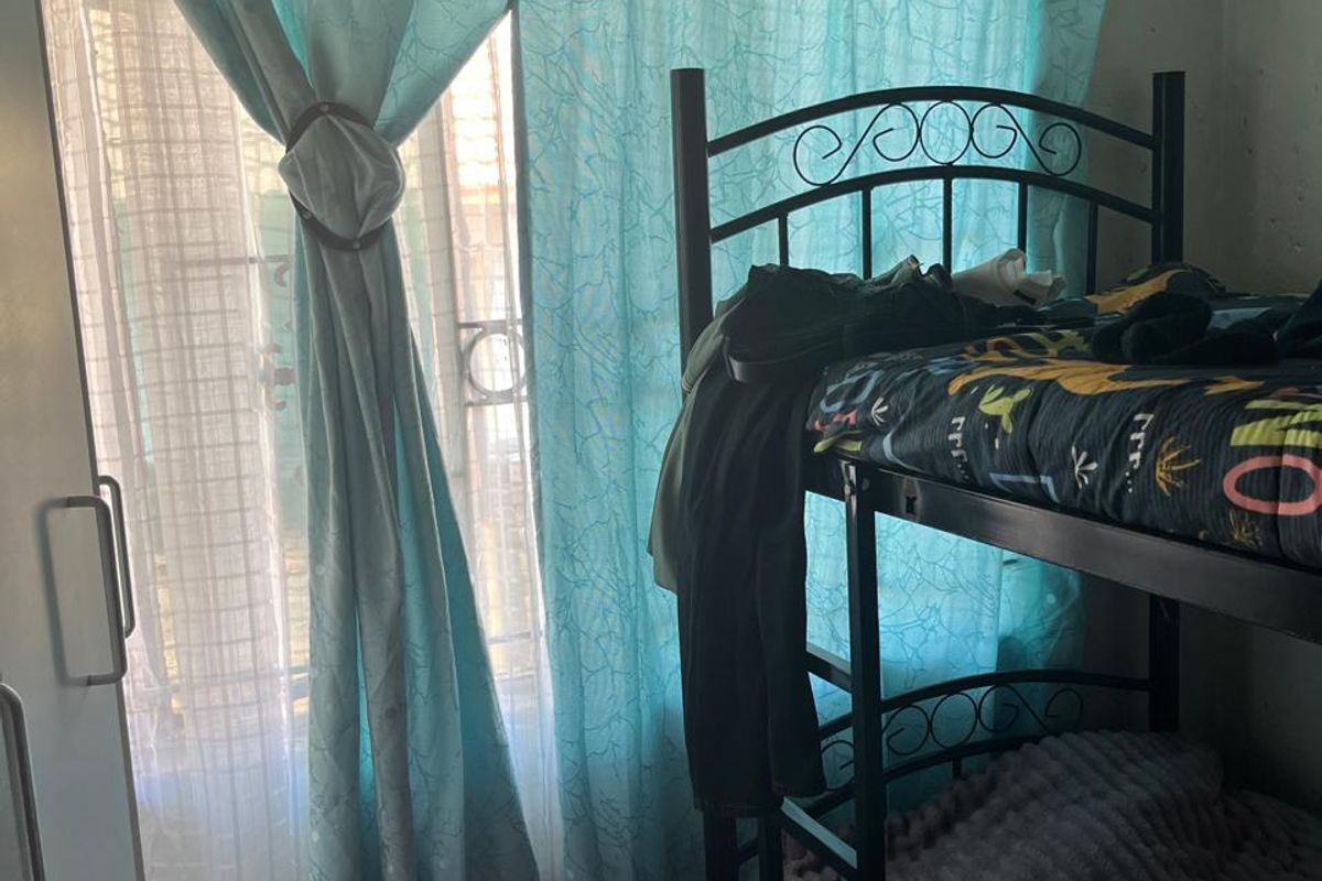 A bedroom featuring a window with a security gate and a built-in cupboard, showing signs of wear and requiring maintenance.