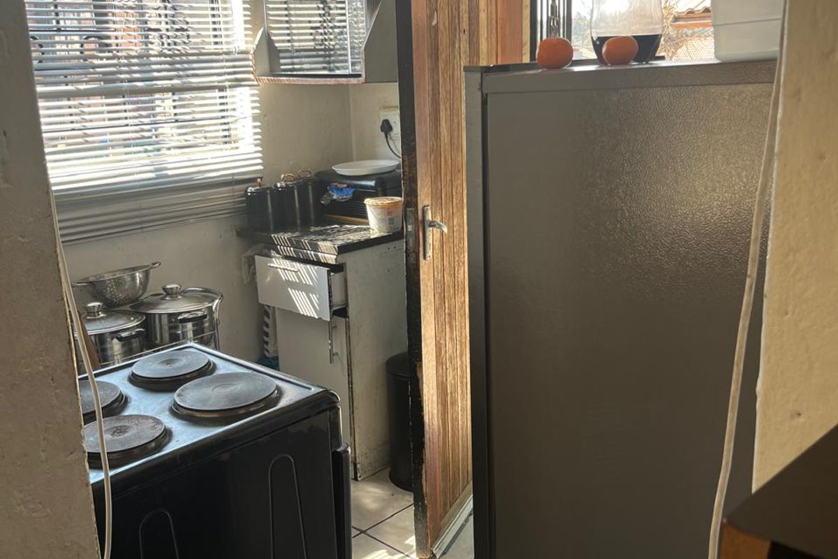 A compact kitchen area featuring tiled flooring, an electric stove, and built-in shelving, with direct access to an exterior door.