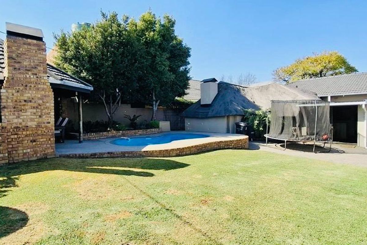 Rear garden featuring a swimming pool, paved patio area, brick chimney, and a mix of thatched and tiled roof structures.