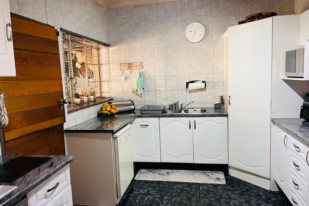 A functional kitchen featuring white cabinetry, dark laminate countertops, tiled backsplash, and dark floor tiles with a built-in pantry cupboard.