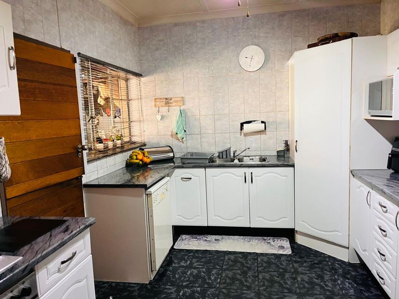 A functional kitchen featuring white cabinetry, dark laminate countertops, tiled backsplash, and dark floor tiles with a built-in pantry cupboard.