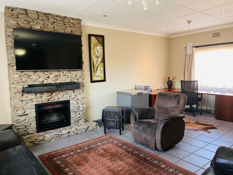 A living room featuring a prominent stone-clad fireplace, tiled flooring, and recessed ceiling lighting, offering a functional space with integrated heating elements.