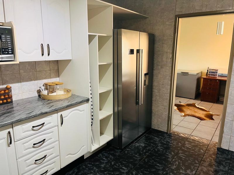 A functional scullery area featuring white cabinetry, stone countertops, tiled backsplash, and dark floor tiles, providing additional storage and prep space.