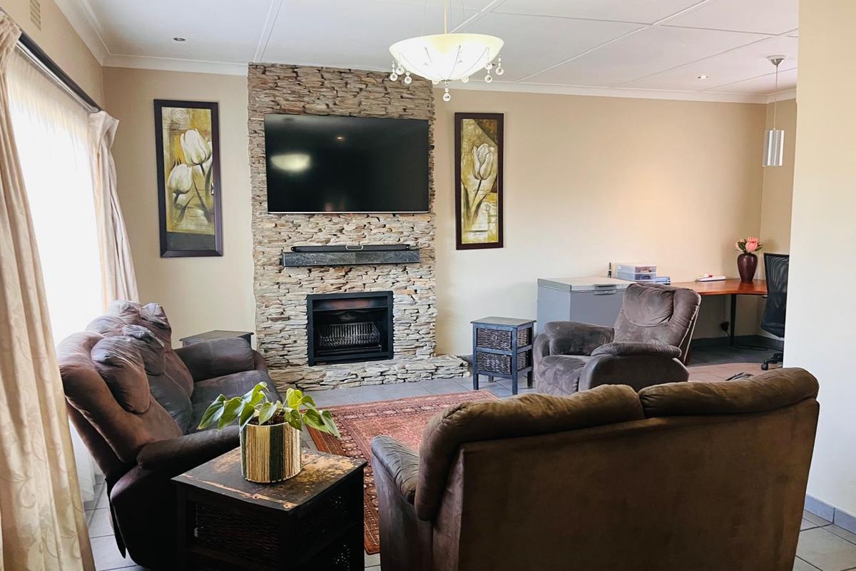 A comfortable living room featuring a prominent stone-clad fireplace, tiled flooring, and recessed ceiling lighting, creating a warm and inviting atmosphere.