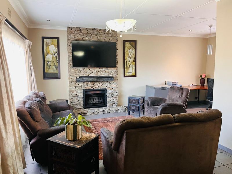 A comfortable living room featuring a prominent stone-clad fireplace, tiled flooring, and recessed ceiling lighting, creating a warm and inviting atmosphere.