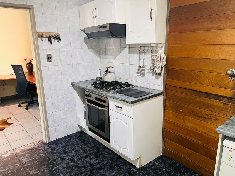 Compact kitchen featuring built-in oven, gas hob, extractor fan, tiled splashback, and dark tiled flooring, offering a functional prep and cooking space.