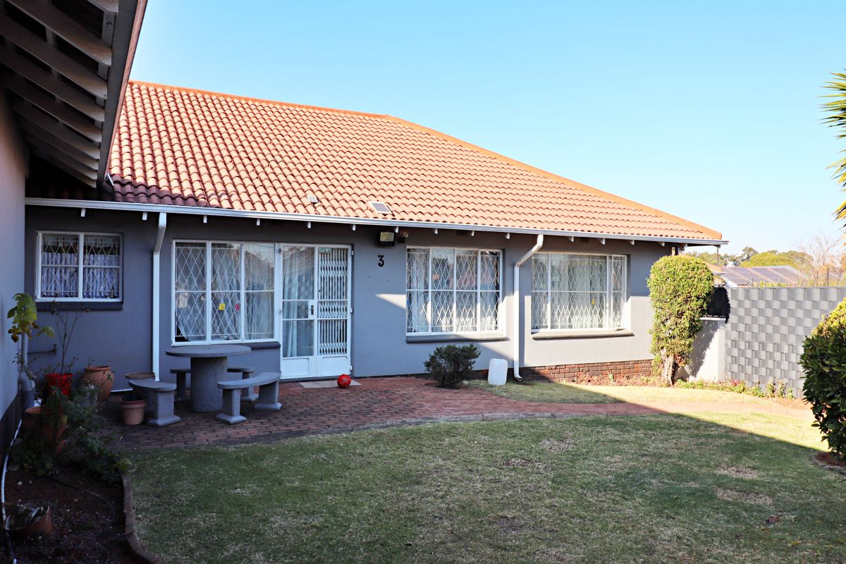 Rear view of the house featuring a tiled roof, brick paved patio area, and secure window bars, overlooking a small garden space.