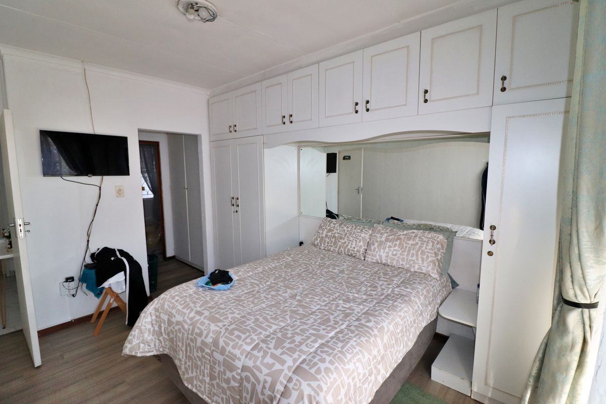 A bedroom featuring extensive white built-in cupboards with integrated storage and a mirrored headboard section, complemented by light-toned laminate flooring.