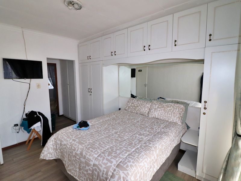 A bedroom featuring extensive white built-in cupboards with integrated storage and a mirrored headboard section, complemented by light-toned laminate flooring.