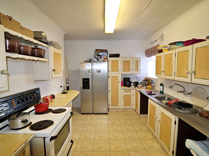 A functional kitchen featuring dated cabinetry, tiled flooring, and a standard electric stove, offering potential for a modern renovation.