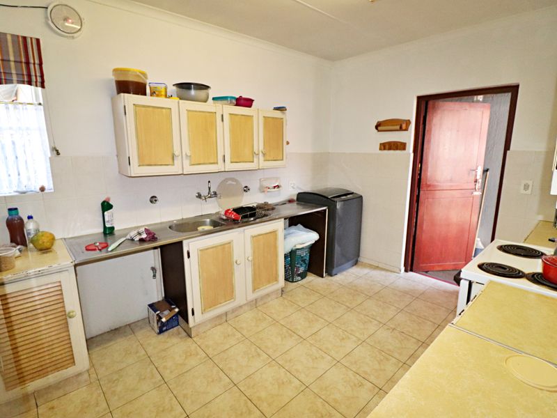 A functional kitchen featuring tiled flooring, built-in cabinetry, a stainless steel sink, and an electric stove, offering potential for modernization.