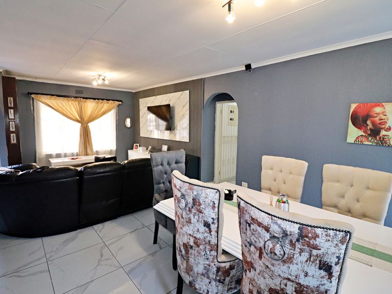 Open plan living and dining area featuring tiled flooring, a decorative feature wall with integrated television mount, and classic archway transitions.