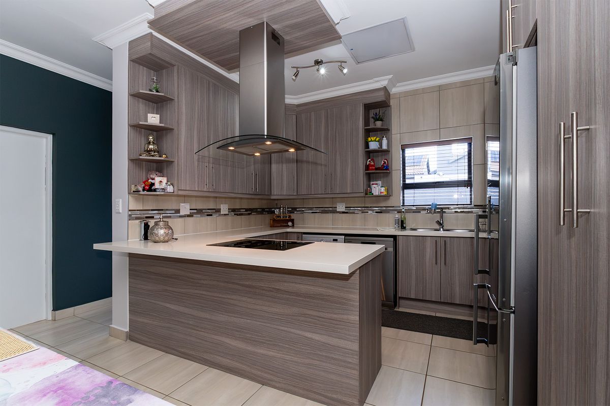 Modern kitchen featuring wood-grain cabinetry, stone countertops, a central extractor fan, and a tiled backsplash with integrated sink and hob.