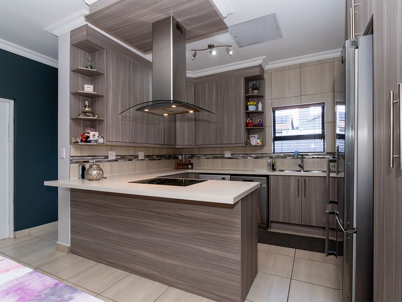 Modern kitchen featuring wood-grain cabinetry, stone countertops, a central extractor fan, and a tiled backsplash with integrated sink and hob.