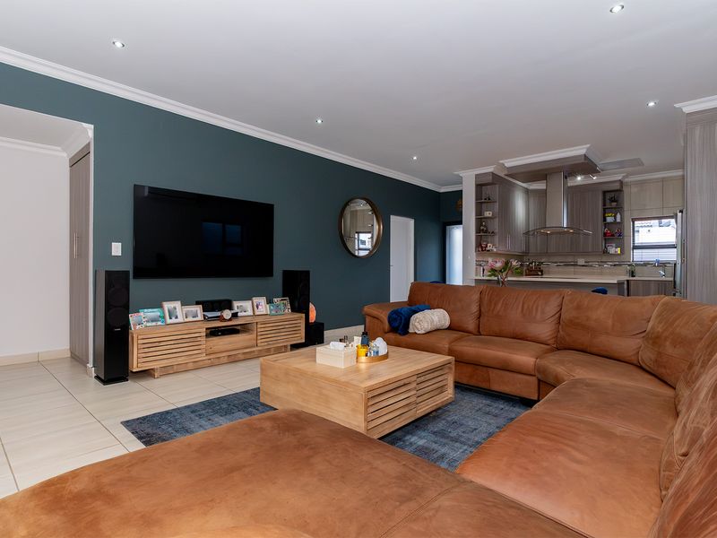 A spacious open-plan living area featuring modern kitchen cabinetry, a stainless steel extractor fan, recessed downlighting, and neutral tiled flooring throughout.