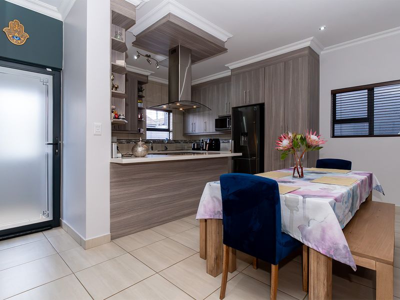 Modern open-plan kitchen and dining area featuring contemporary wood-grain cabinetry, stone countertops, stainless steel extractor fan, and neutral tiled flooring.