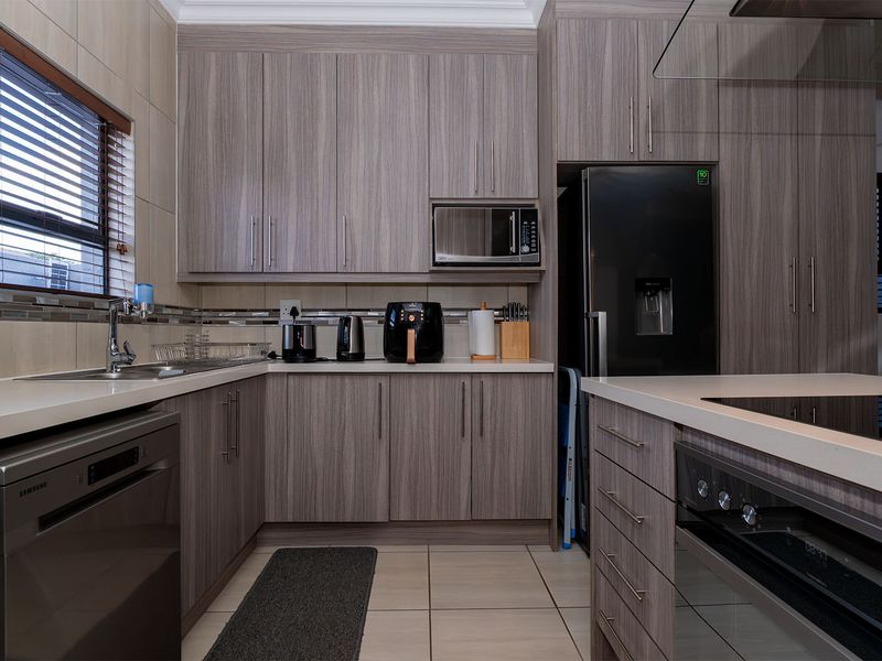 Modern kitchen featuring wood-grain cabinetry, stone countertops, integrated appliances, and tiled finishes, offering a functional and contemporary cooking space.