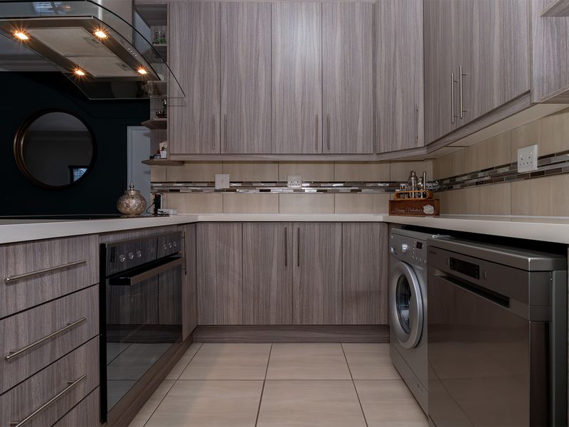 Modern kitchen featuring wood-grain cabinetry, stone countertops, tiled backsplash, and integrated appliances including an oven and extractor fan.