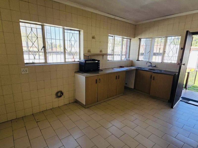 A dated kitchen featuring tiled walls, built-in wooden cabinetry, and a double sink, with direct access to the rear garden area.