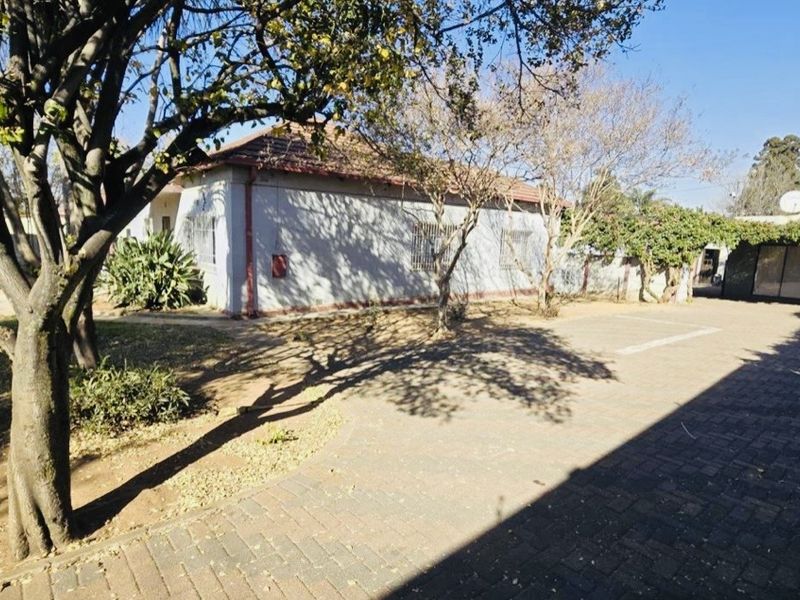 Rear exterior view of the property featuring a paved driveway, established trees, and a secure boundary wall.