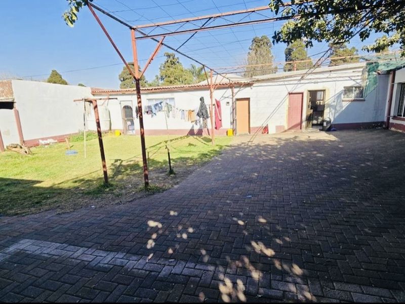 A rear exterior view of the property featuring a paved courtyard, a lawn area, and a metal pergola structure attached to the building.