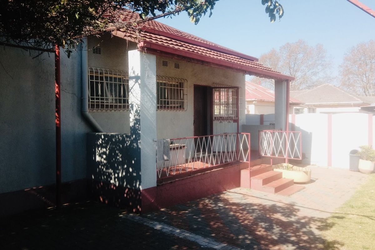 Rear view of the house featuring a covered patio, paved area, and security bars on windows.