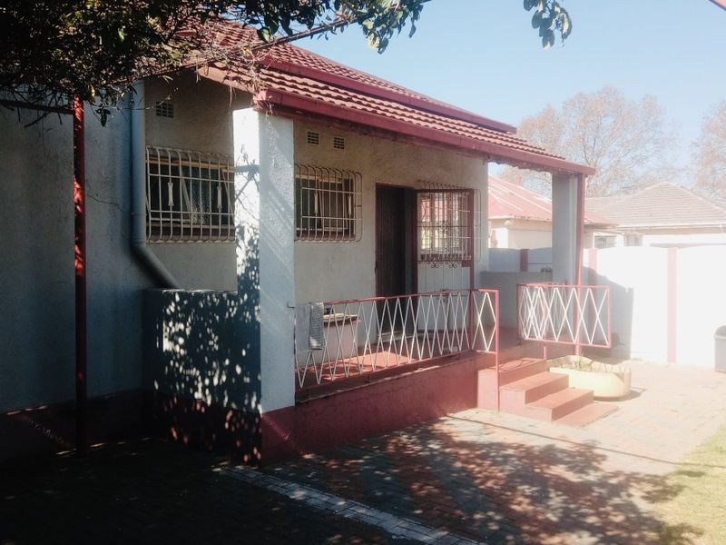 Rear view of the house featuring a covered patio, paved area, and security bars on windows.