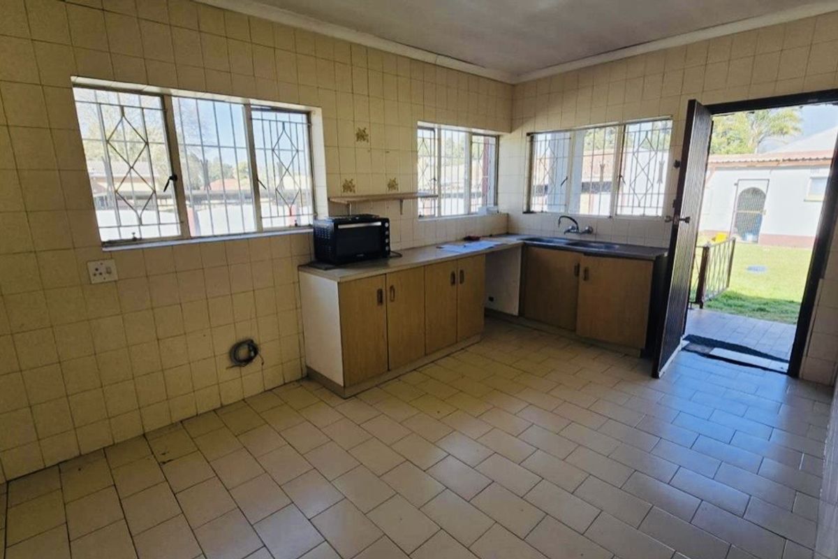 A functional, empty kitchen featuring tiled walls and floors, built-in cabinetry, and direct access to the rear garden area.