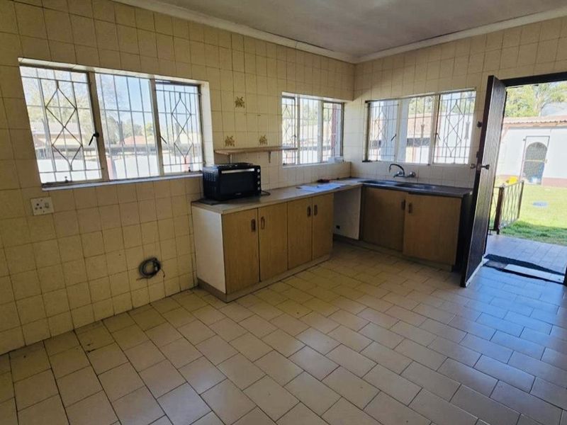 A functional, empty kitchen featuring tiled walls and floors, built-in cabinetry, and direct access to the rear garden area.