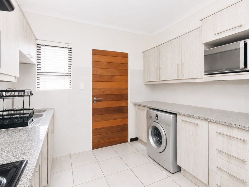 A functional scullery featuring light wood-finish cabinetry, granite countertops, a stainless steel sink, and space for a washing machine.