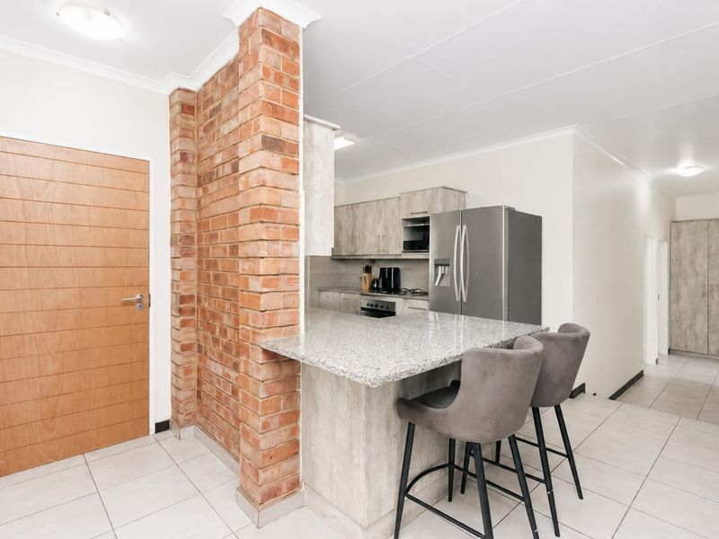 Open plan kitchen featuring a granite breakfast bar, exposed brick feature pillar, and modern laminated cabinetry with integrated appliances.