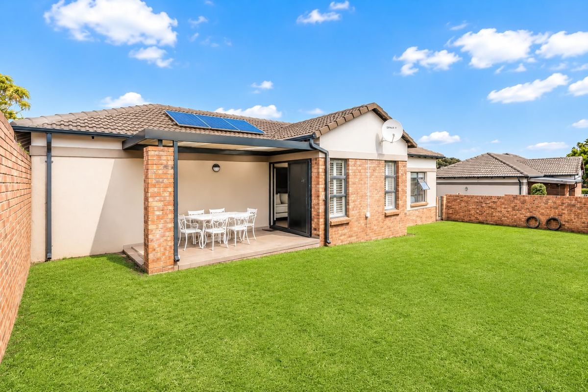 Rear view of the townhouse featuring a covered patio, brick exterior, solar panels, and a well-maintained private garden with boundary walls.