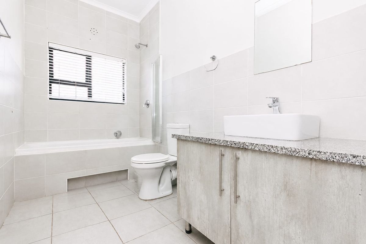 A clean, neutral-toned bathroom featuring a built-in vanity with a granite countertop, vessel sink, and a combined bathtub and shower area.
