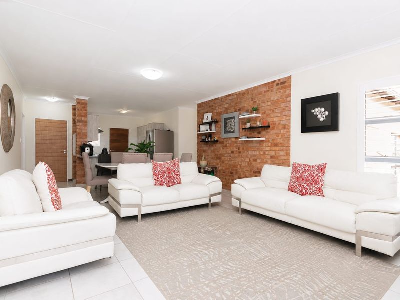 Spacious open-plan living and dining area featuring a prominent exposed brick feature wall, neutral tiled flooring, and abundant natural light.