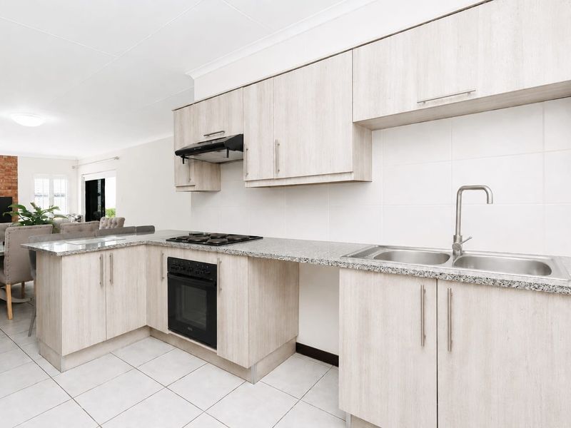 Modern open-plan kitchen featuring light wood-finish cabinetry, granite countertops, a double basin sink, and integrated cooking appliances, flowing into the adjacent living area.
