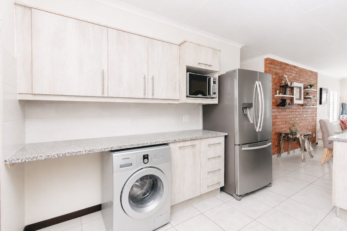 Modern kitchen area featuring light wood-finish cabinetry, granite-look countertops, built-in microwave, and a striking exposed brick feature wall in the adjacent living space.