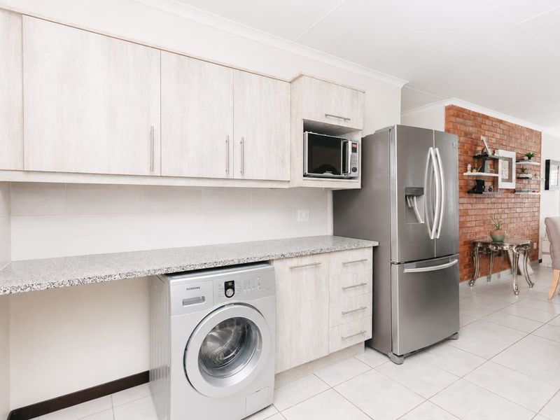 Modern kitchen area featuring light wood-finish cabinetry, granite-look countertops, built-in microwave, and a striking exposed brick feature wall in the adjacent living space.