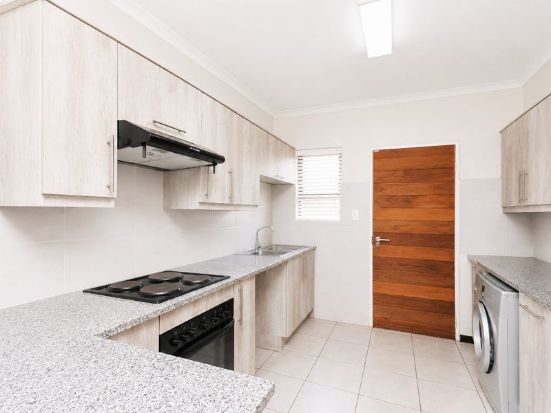A clean, modern kitchen featuring light wood-grain cabinetry, granite countertops, integrated electric hob and oven, and tiled flooring.
