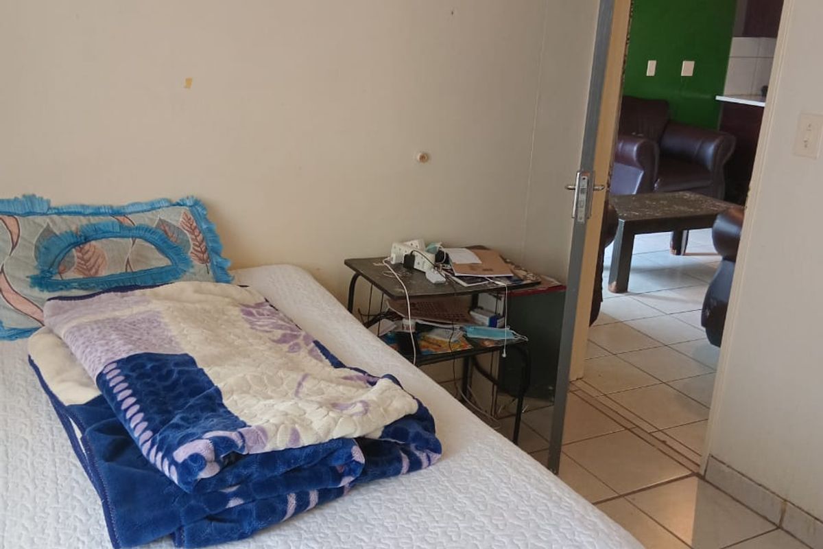 A bedroom featuring tiled flooring and an internal door leading to an adjacent living area, showing signs of wear on the wall surfaces.