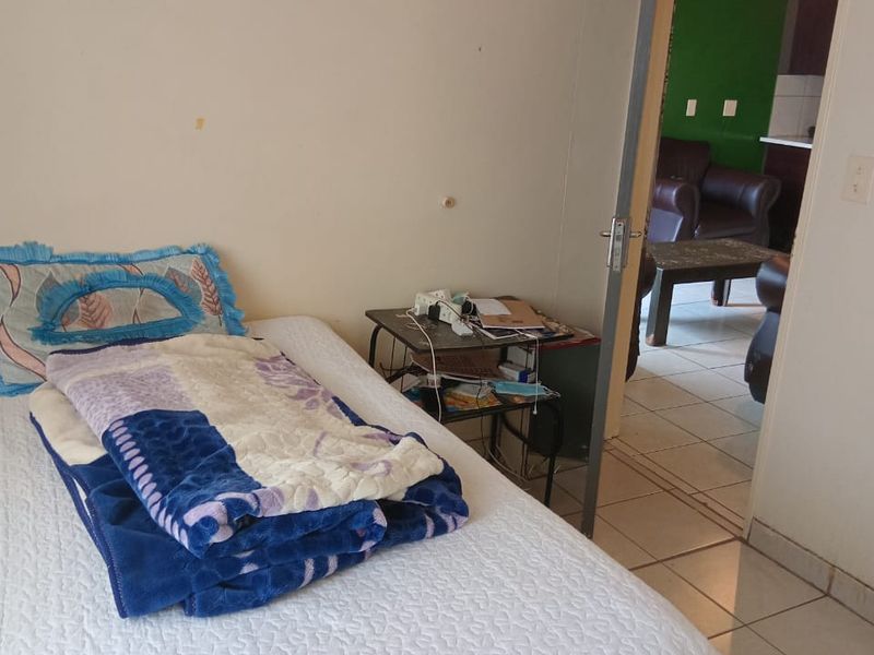 A bedroom featuring tiled flooring and an internal door leading to an adjacent living area, showing signs of wear on the wall surfaces.