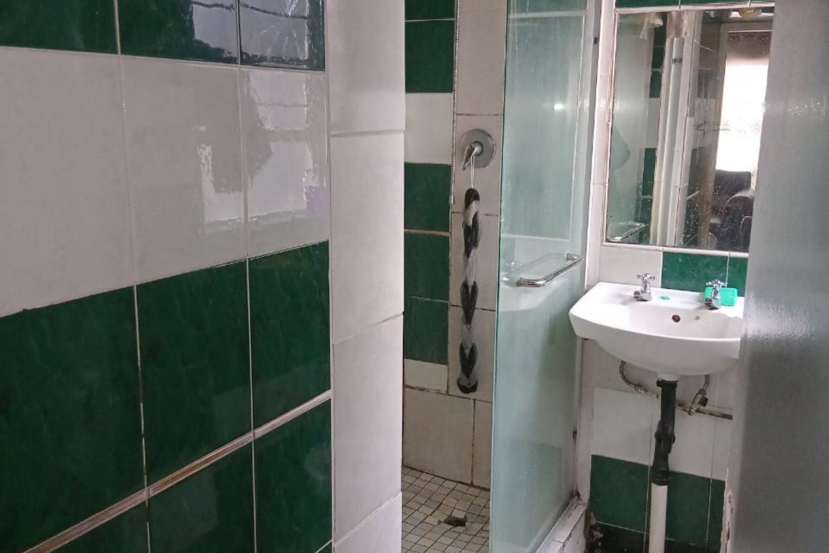 A dated bathroom featuring a shower enclosure and wall-mounted basin, requiring significant renovation and repair to the ceiling and tiling.