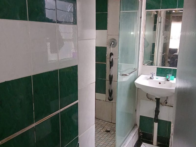 A dated bathroom featuring a shower enclosure and wall-mounted basin, requiring significant renovation and repair to the ceiling and tiling.