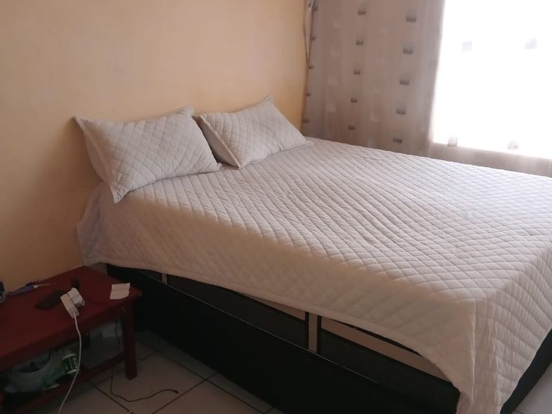 A simple bedroom featuring tiled flooring and natural light from a window.