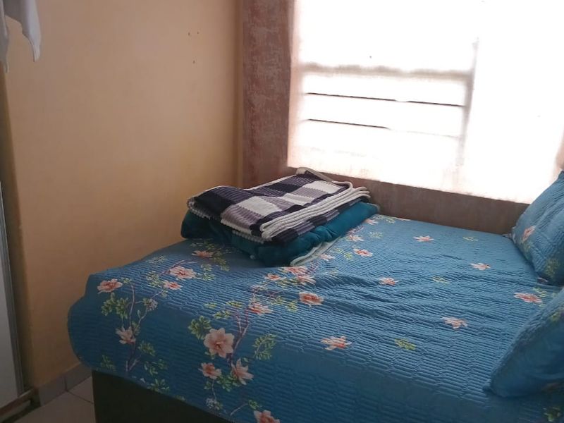A compact bedroom featuring tiled flooring and a horizontal window, currently requiring cosmetic updates to the wall finishes.